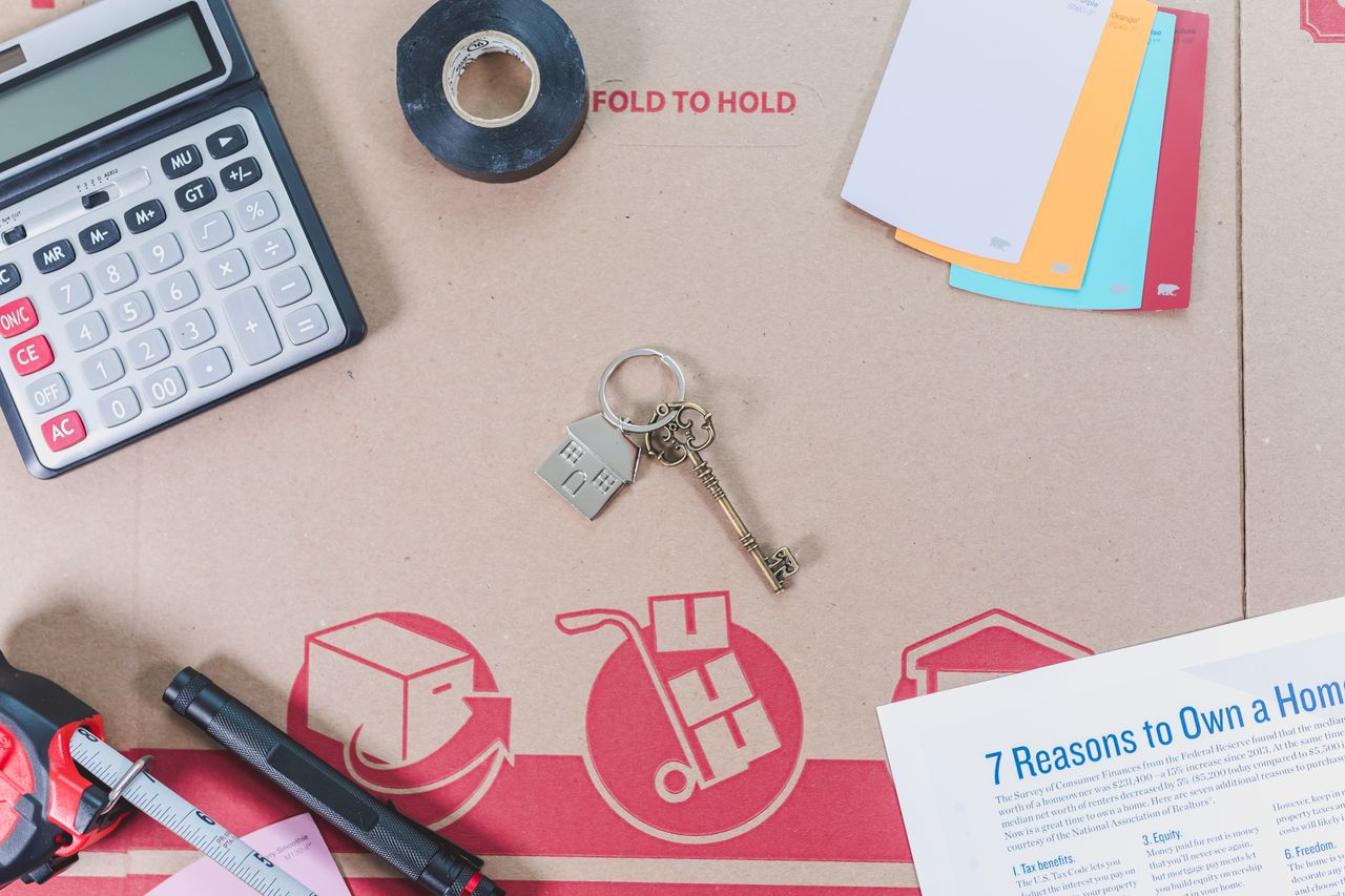 gallery-1 Flat lay of home buying essentials with calculator, keys, tape, and color swatches.