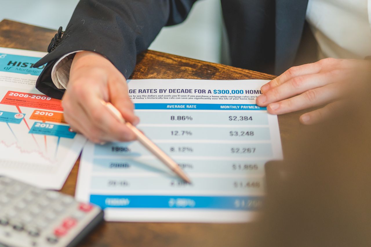 our-services-1 A close-up of hands analyzing mortgage rate documents with a pen and calculator in a business setting.