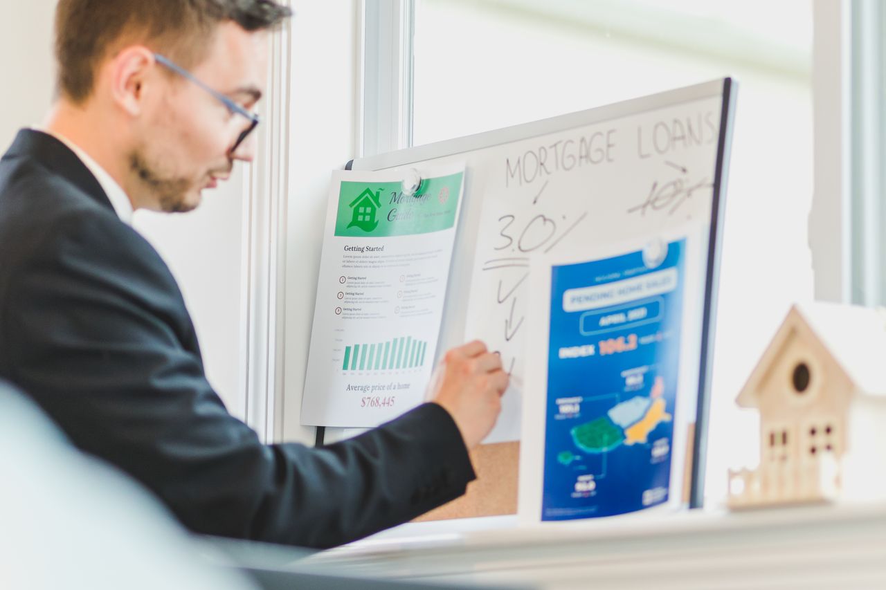 gallery-3 Real estate agent analyzing mortgage loan details on a whiteboard in an office setting.
